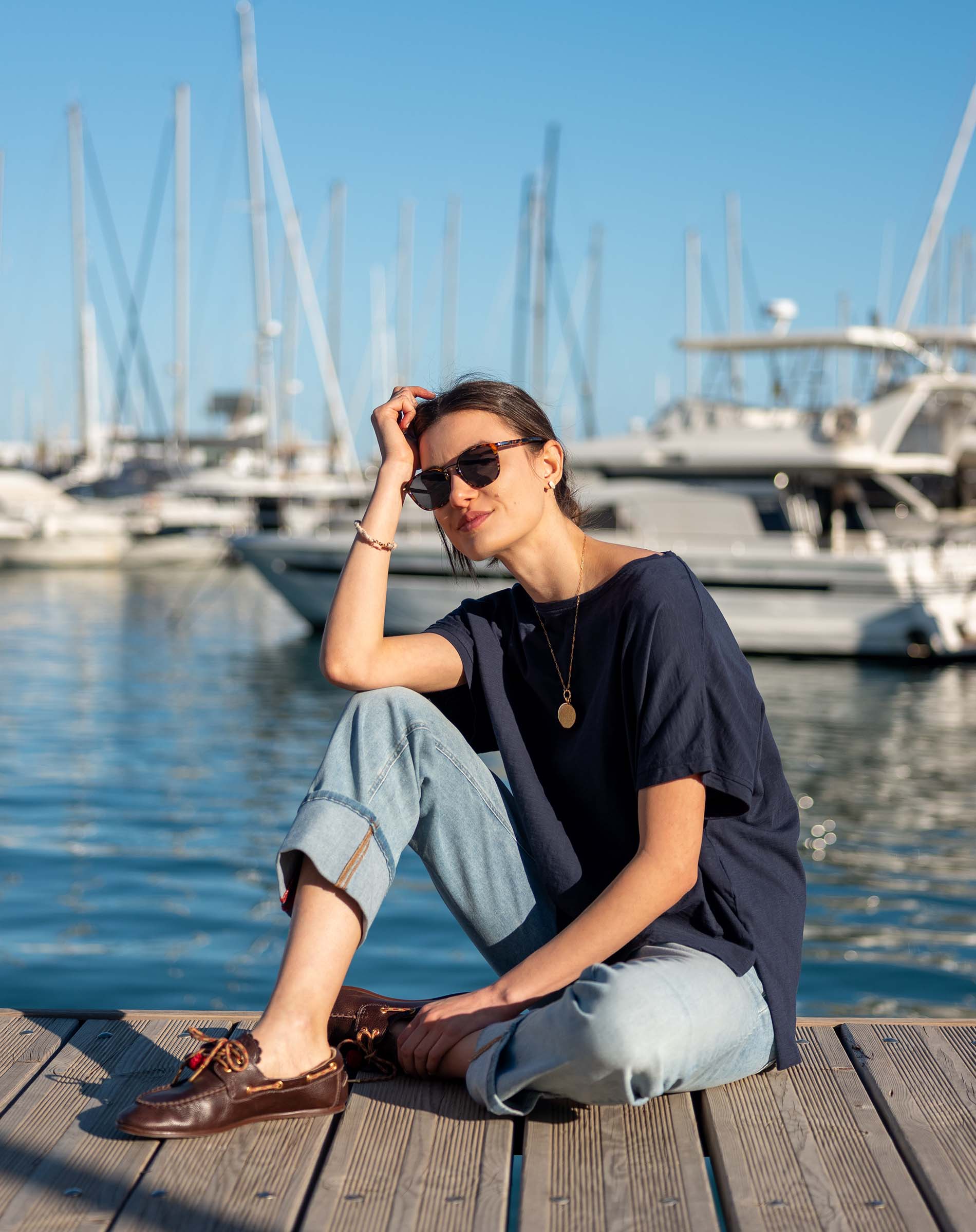 Navy blue oversized short-sleeve tee worn by a model on a dock near a boat harbor.
