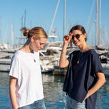 Travel-friendly model wearing a navy short-sleeve tee with loose fit and two women in a harbor setting.