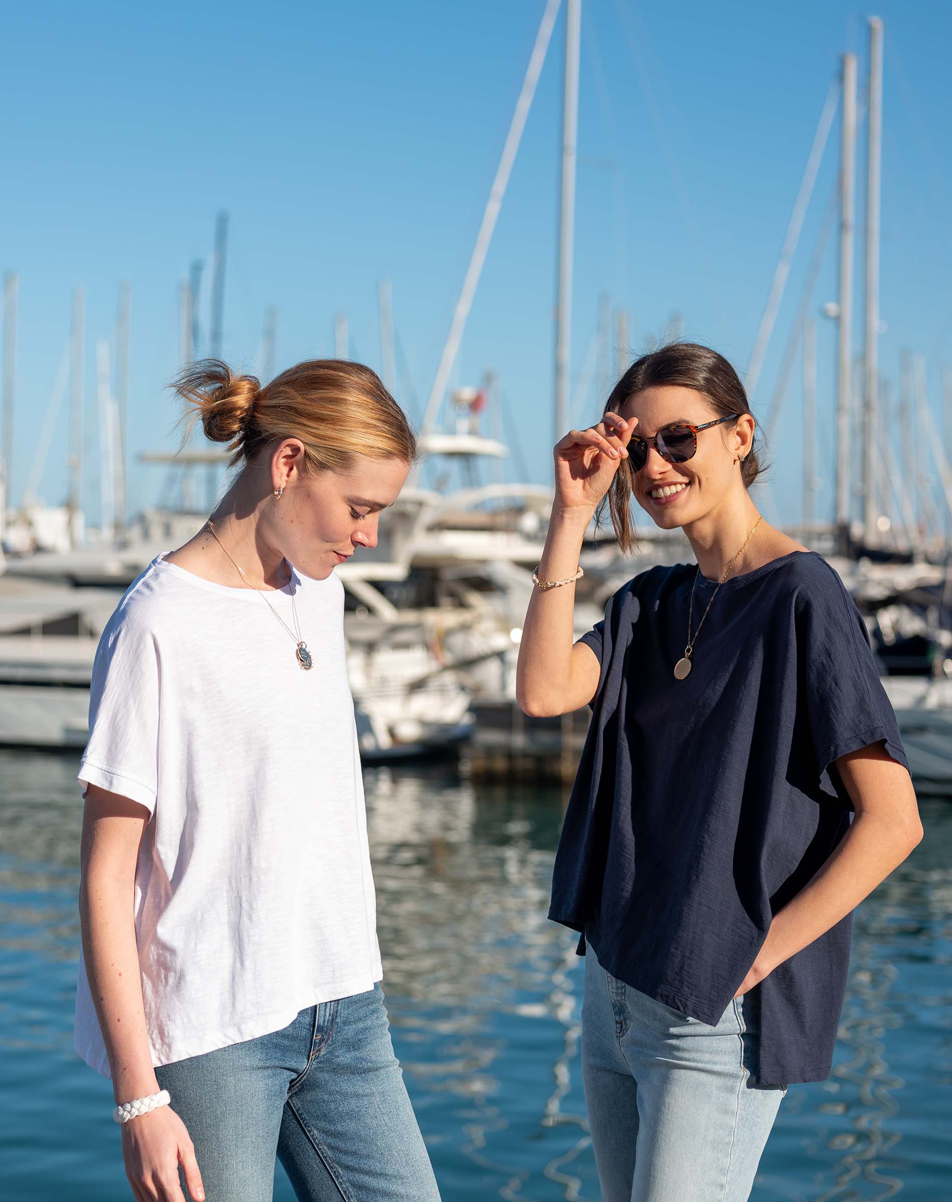 Travel-friendly model wearing a navy short-sleeve tee with loose fit and two women in a harbor setting.