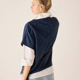 Woman wearing a navy sweater over a white shirt with light blue jeans on a beige background