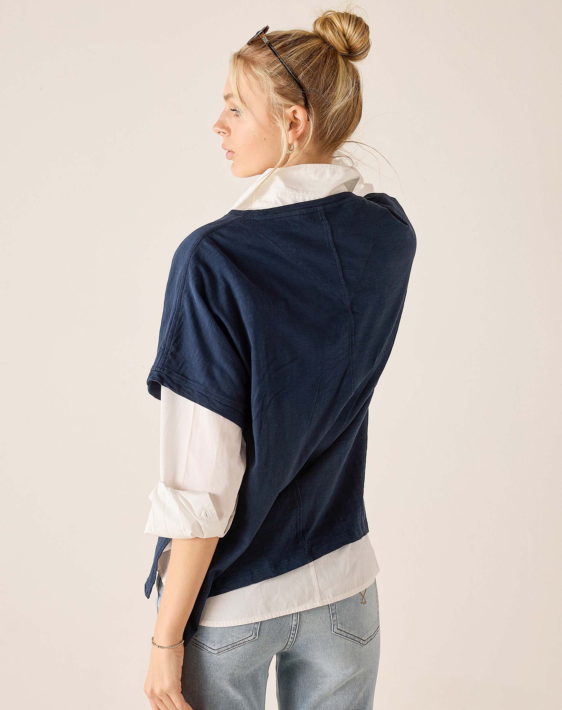 Woman wearing a navy sweater over a white shirt with light blue jeans on a beige background