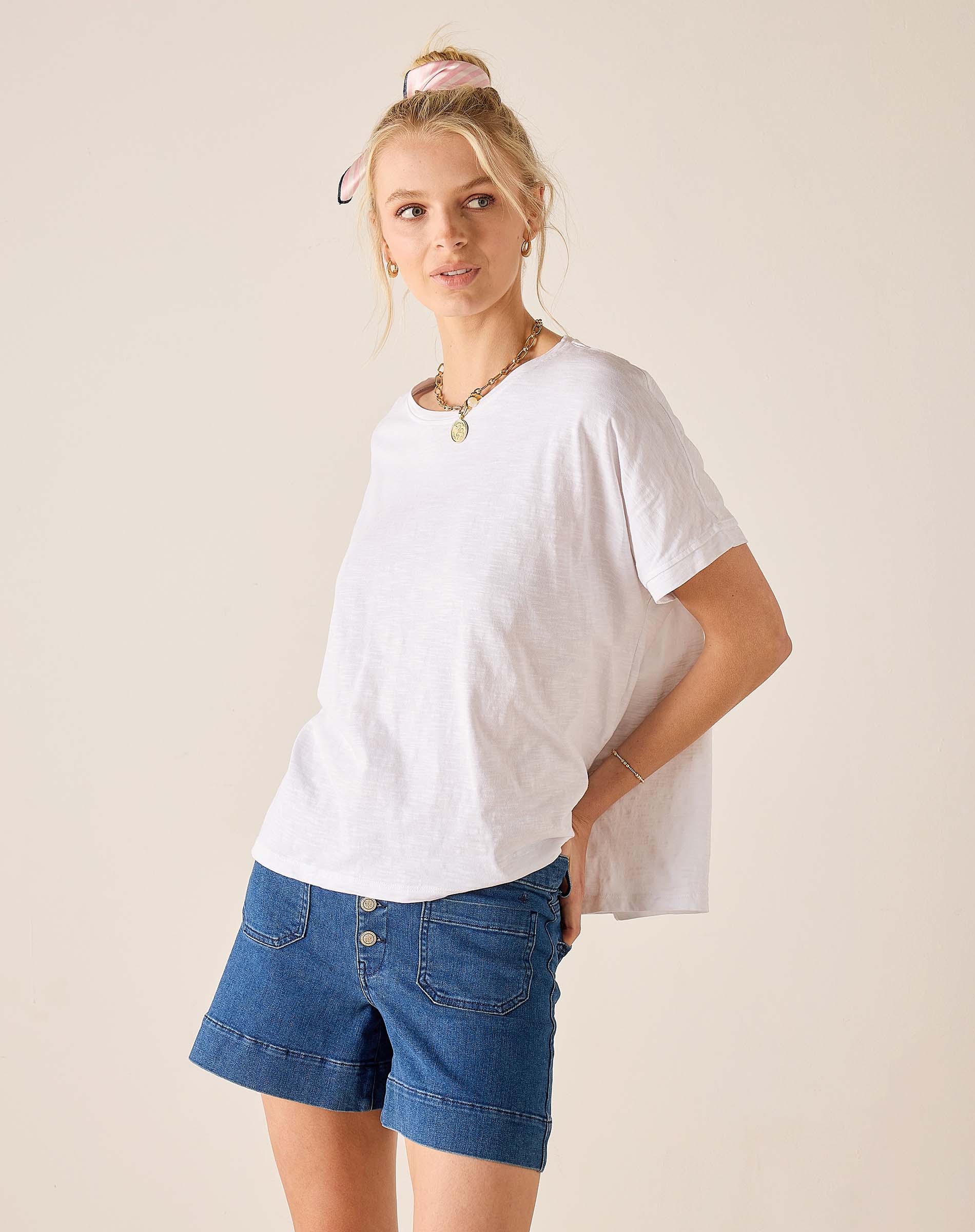 Woman wearing a white t-shirt and blue denim shorts on a beige background