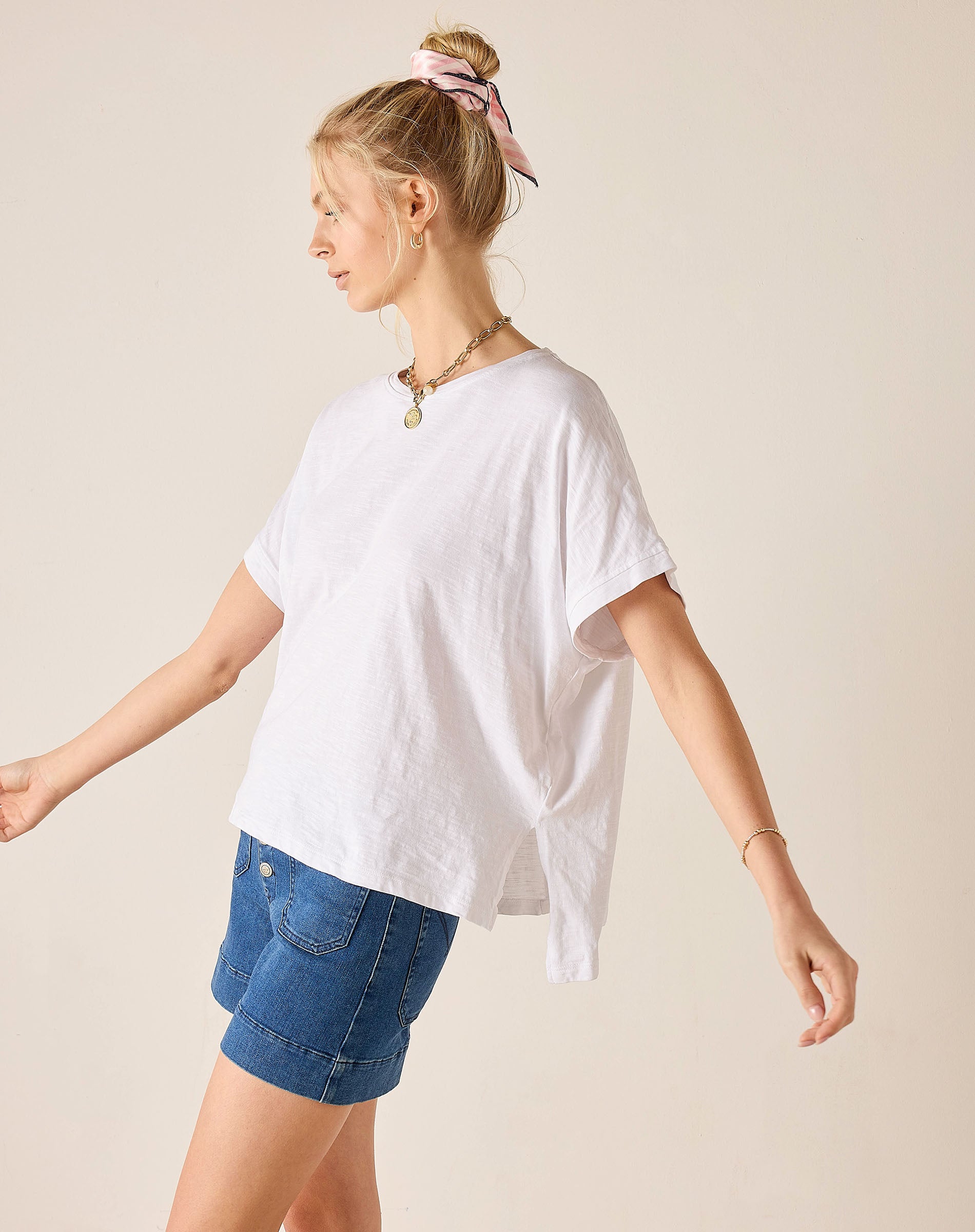 Woman wearing a white oversized t-shirt and denim shorts on a beige background