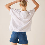 Person wearing a white oversized shirt and blue shorts with a neutral background
