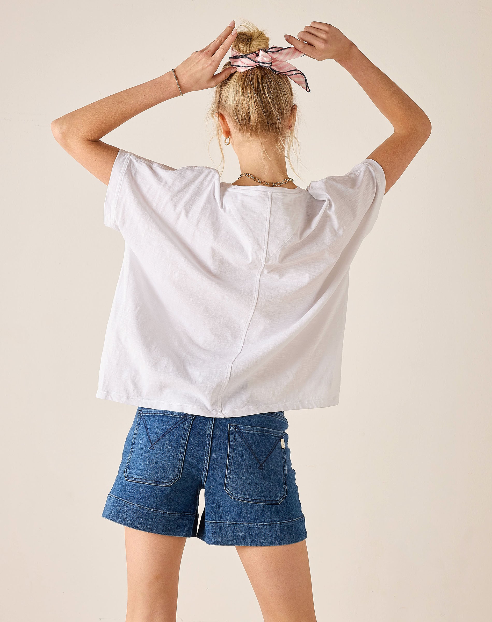 Person wearing a white oversized shirt and blue shorts with a neutral background
