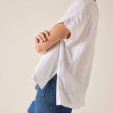 Person wearing a white oversized shirt and blue shorts on a plain background