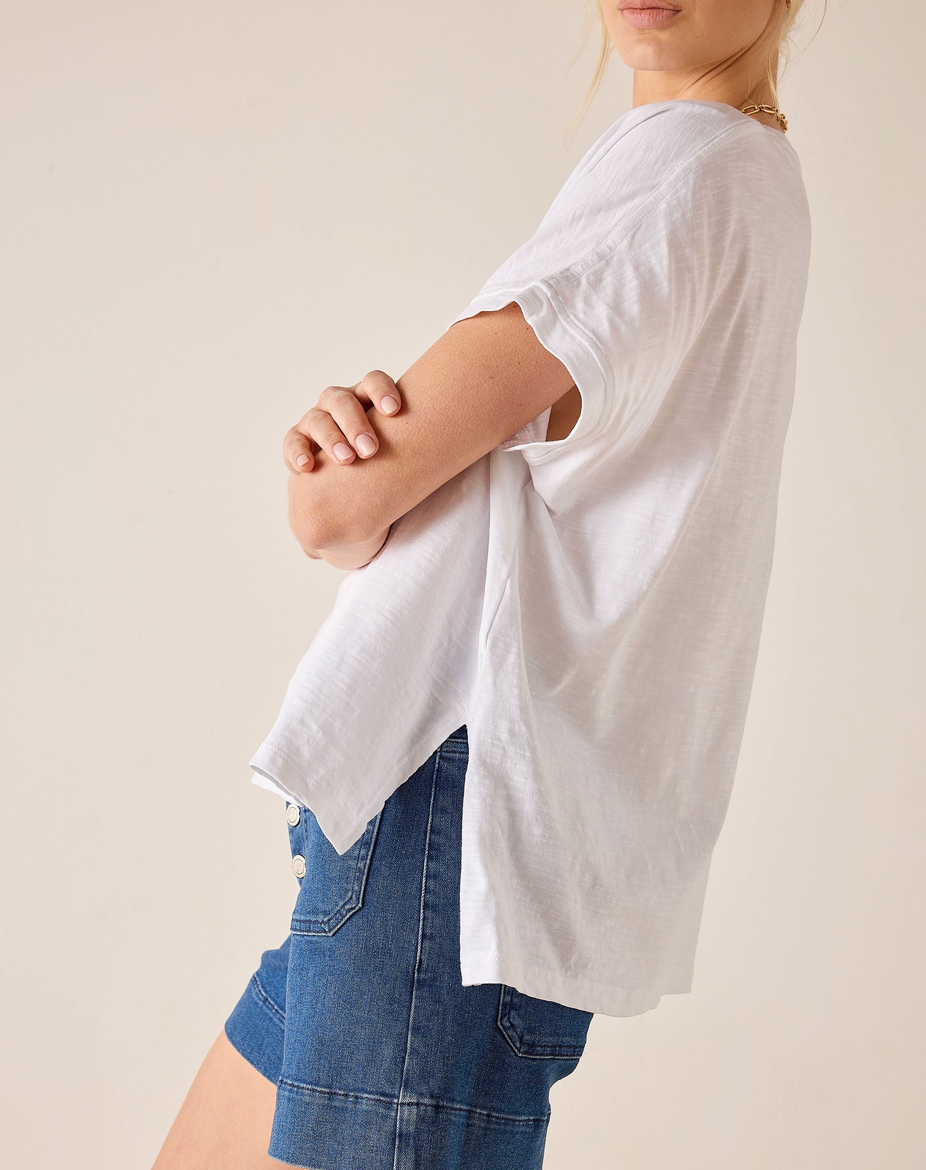 Person wearing a white oversized shirt and blue shorts on a plain background