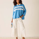 Woman wearing a blue and white striped shirt with white pants against a plain background