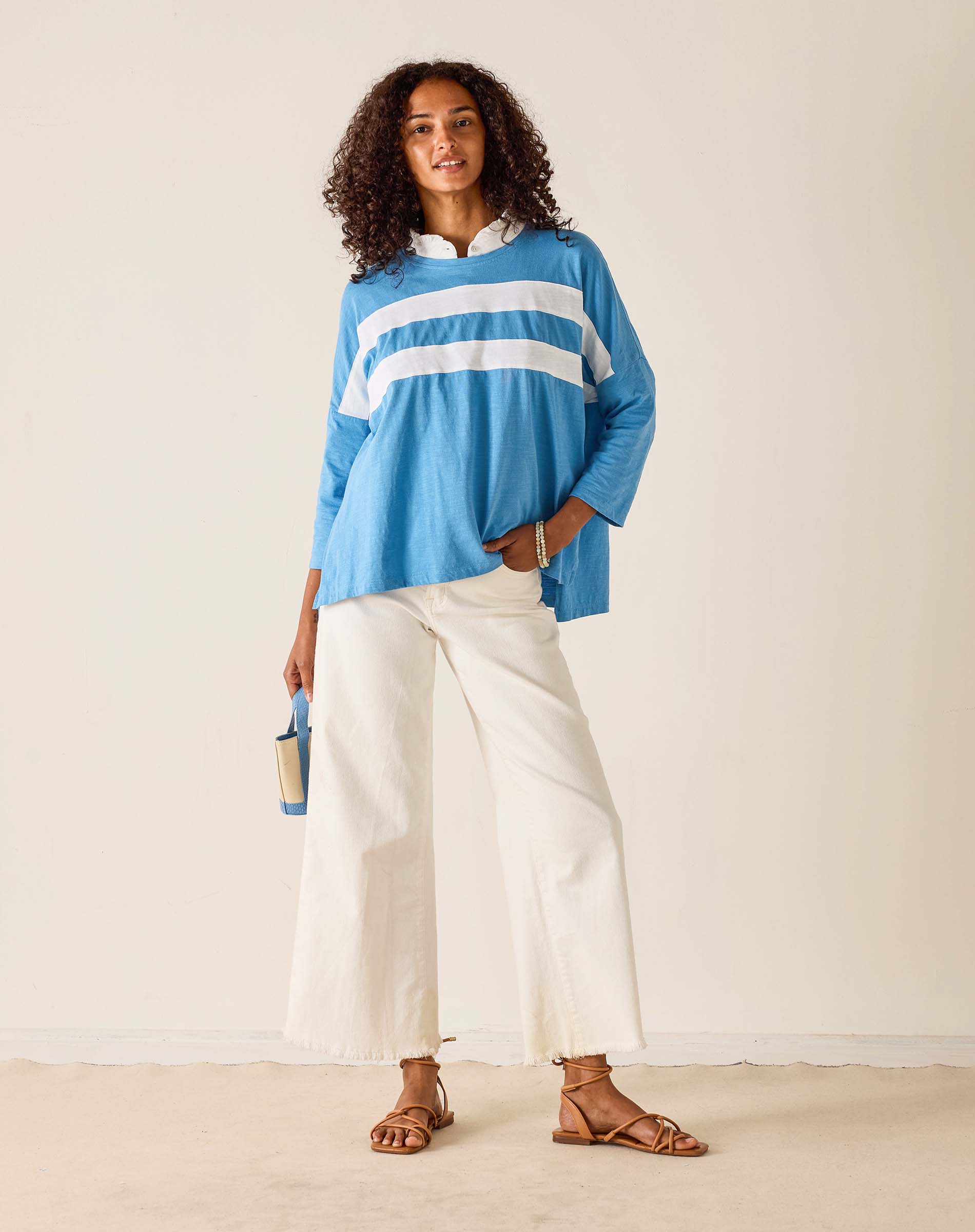 Woman wearing a blue and white striped shirt with white pants against a plain background