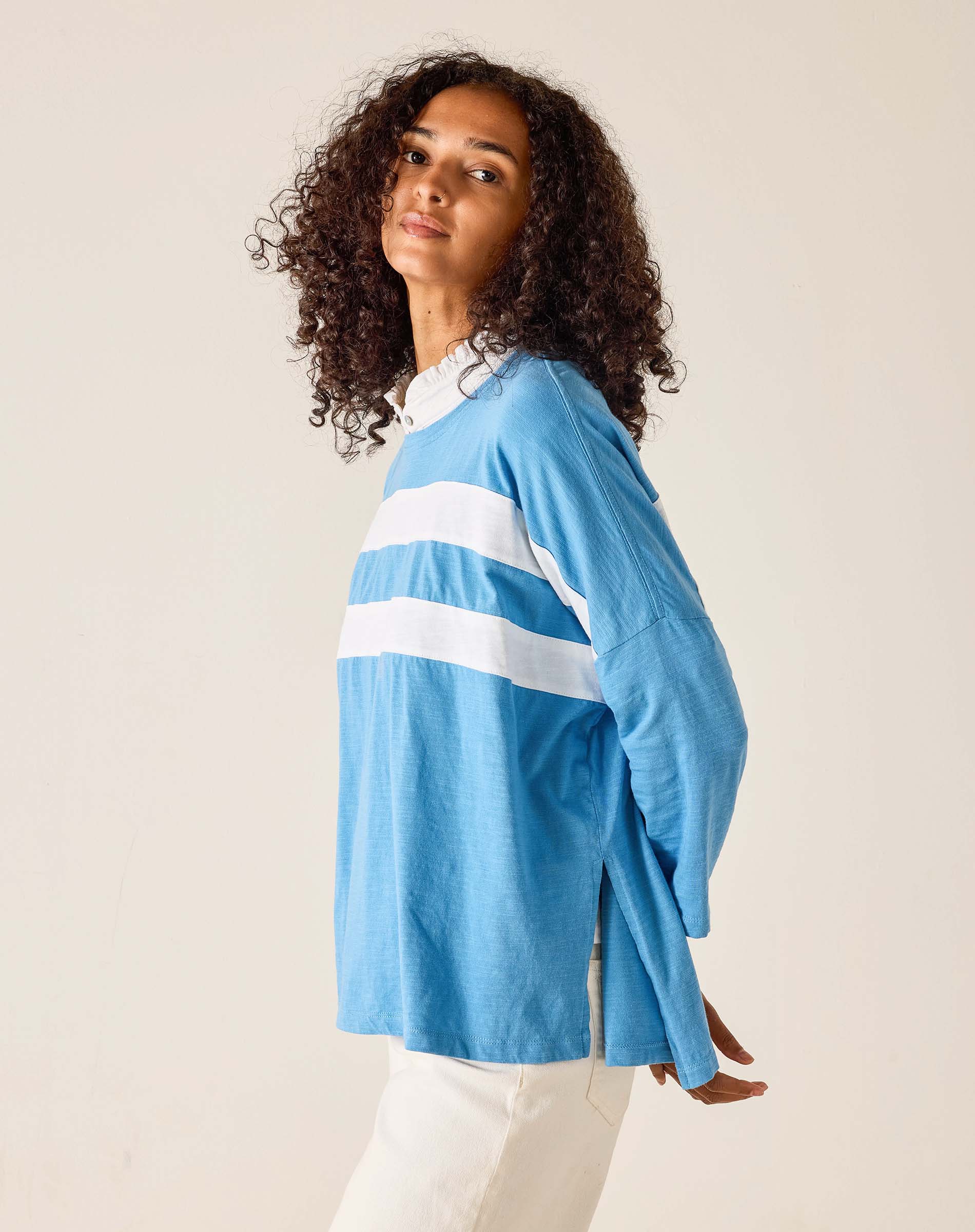Woman wearing a light blue long-sleeve shirt with white stripes on a plain background