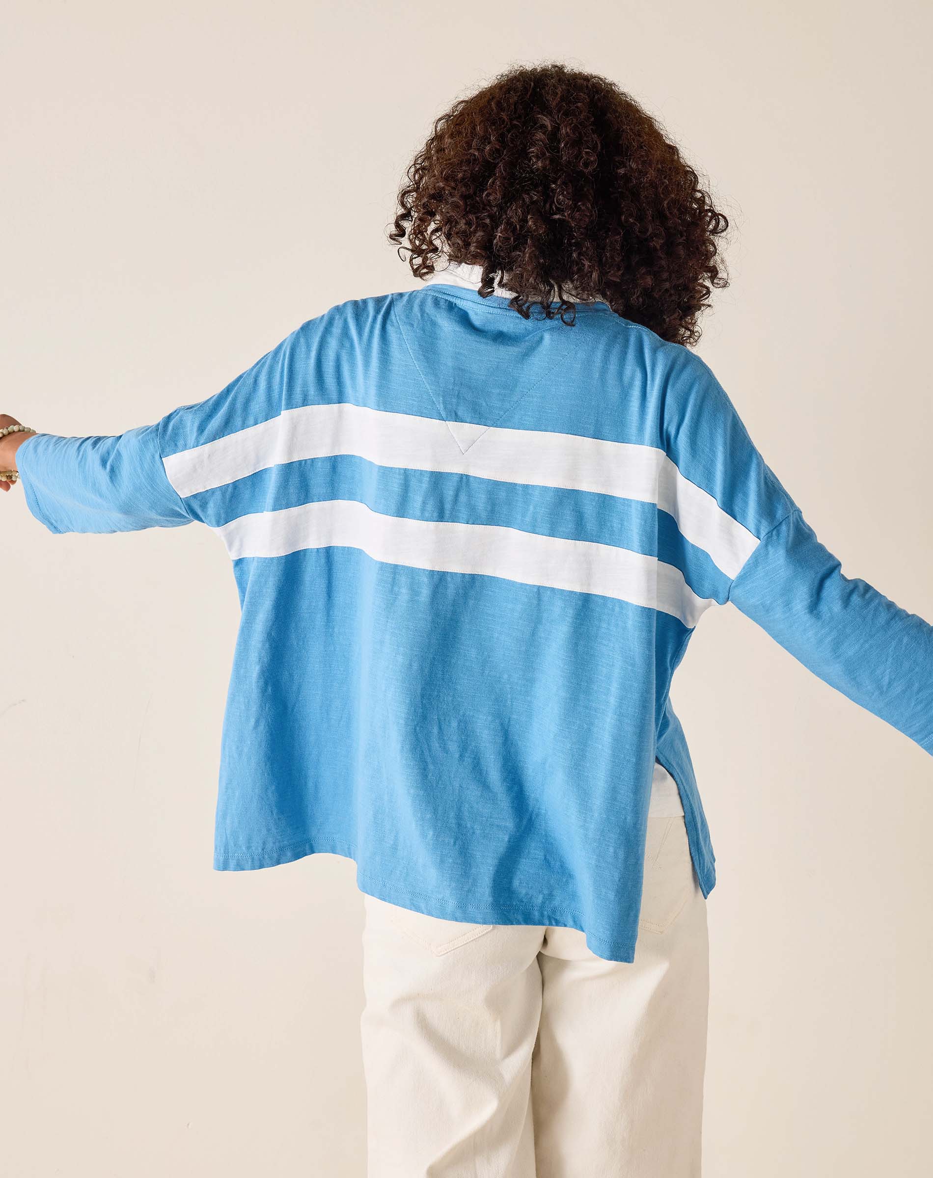 Person wearing a blue cardigan with white stripes from behind on a beige background