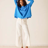 Woman wearing a blue top and white pants against a plain background