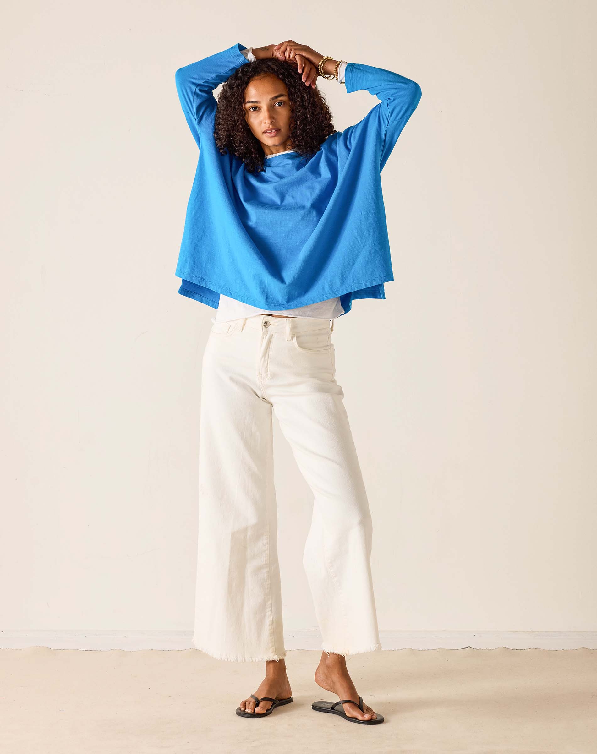 Woman wearing a blue top and white pants against a plain background