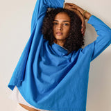 Woman wearing a blue shirt with arms raised against a plain background