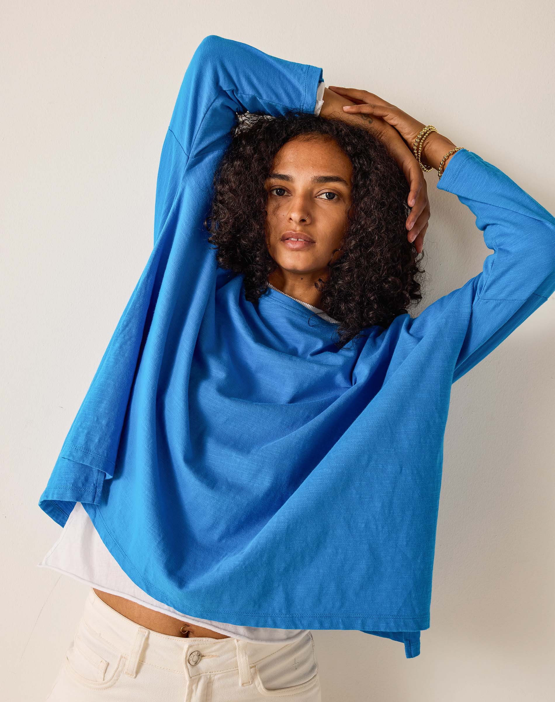 Woman wearing a blue shirt with arms raised against a plain background