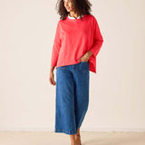 Woman wearing a red top and blue jeans against a plain background