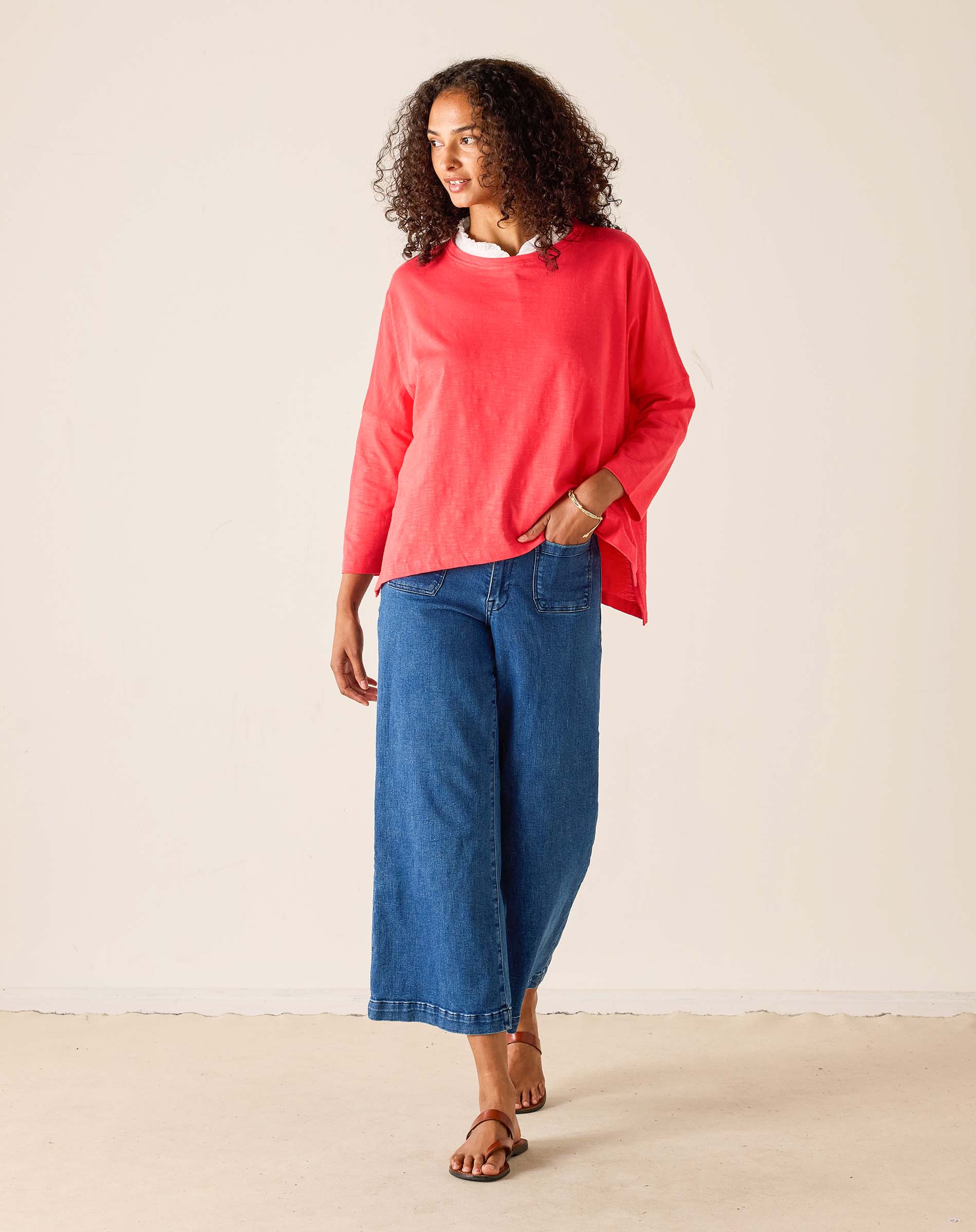 Woman wearing a red top and blue jeans against a plain background