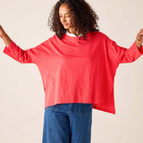 Person wearing a red oversized sweater and blue jeans against a plain background