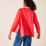 Person wearing a red cardigan and blue jeans on a beige background