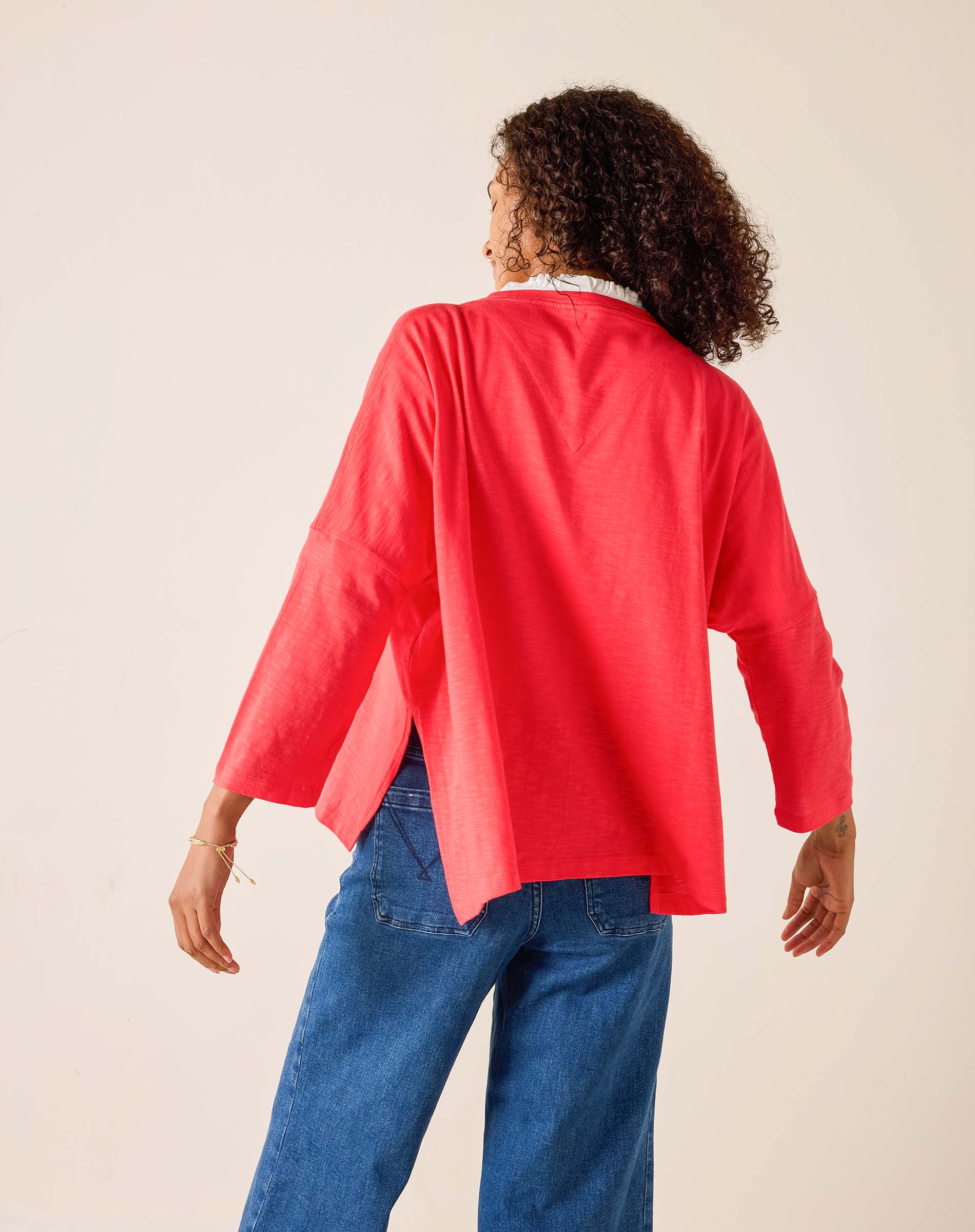 Person wearing a red cardigan and blue jeans on a beige background