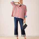 Woman wearing a red and white striped shirt with rolled-up sleeves, blue jeans, and red shoes, holding a black clutch.