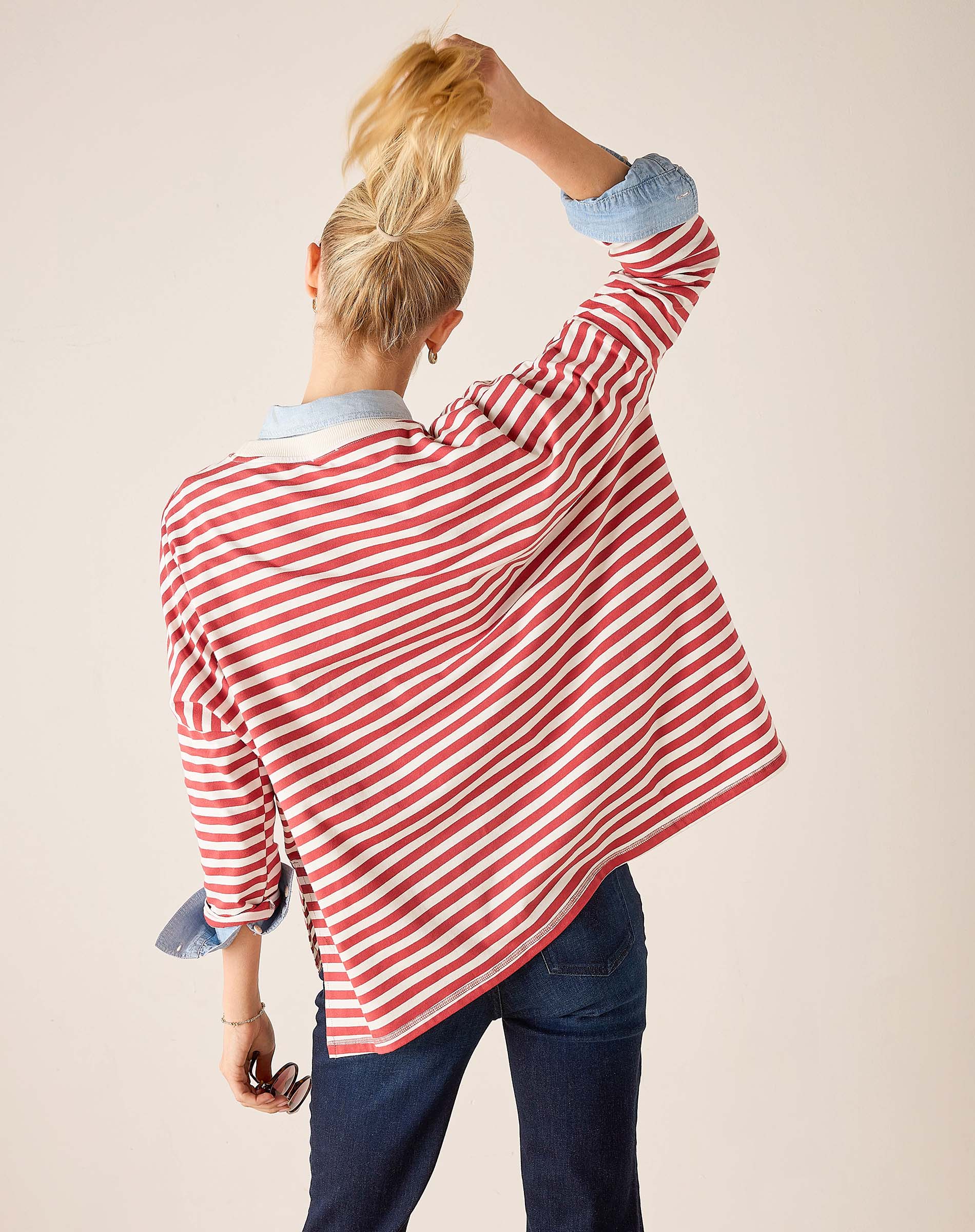Person wearing a red and white striped shirt with rolled-up sleeves on a plain background