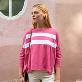 Woman wearing a pink sweater with white stripes against a pink wall.