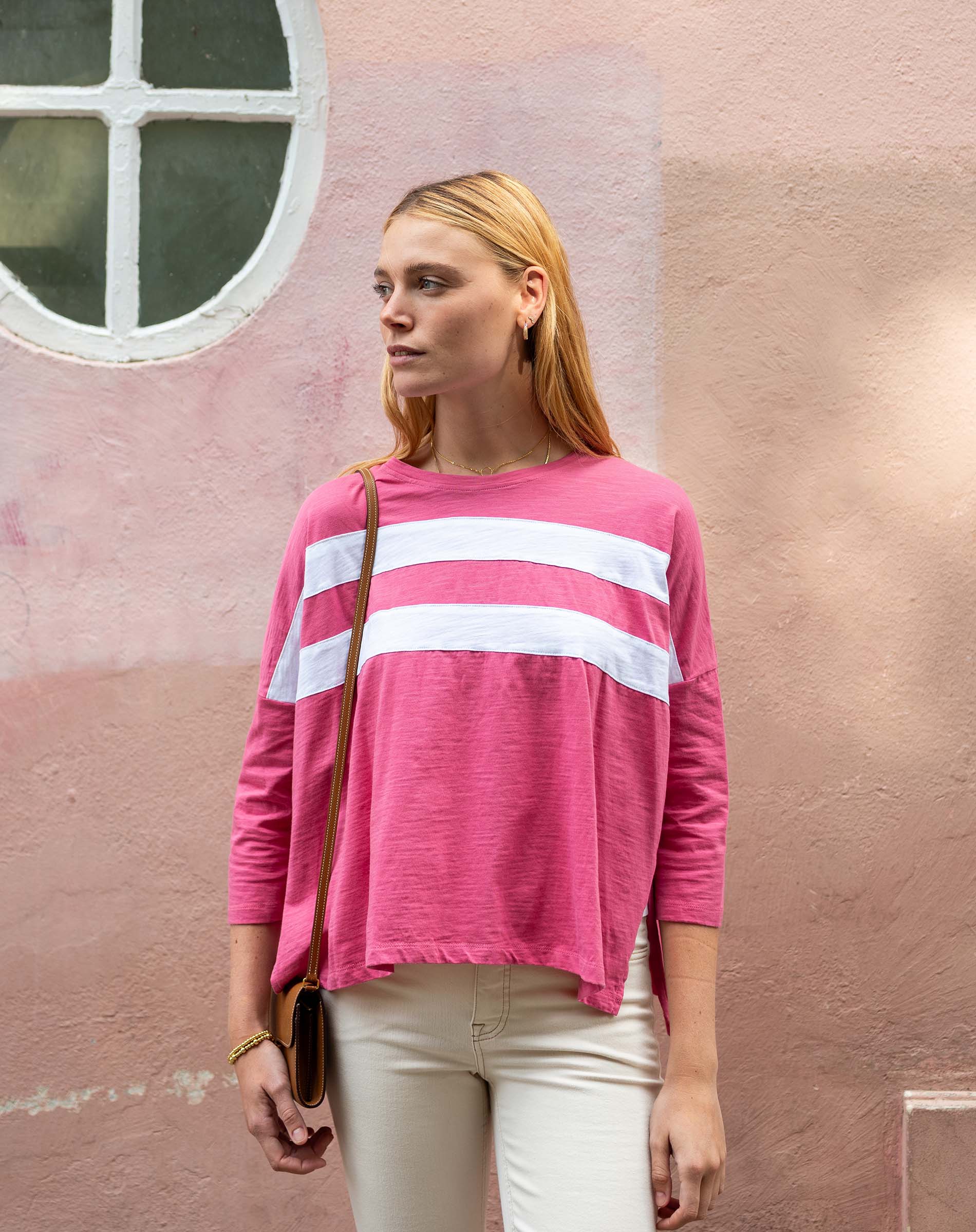 Woman wearing a pink sweater with white stripes against a pink wall.