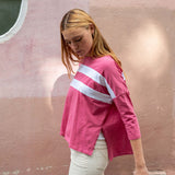 Woman wearing a pink long-sleeve shirt with a white stripe against a pink wall.