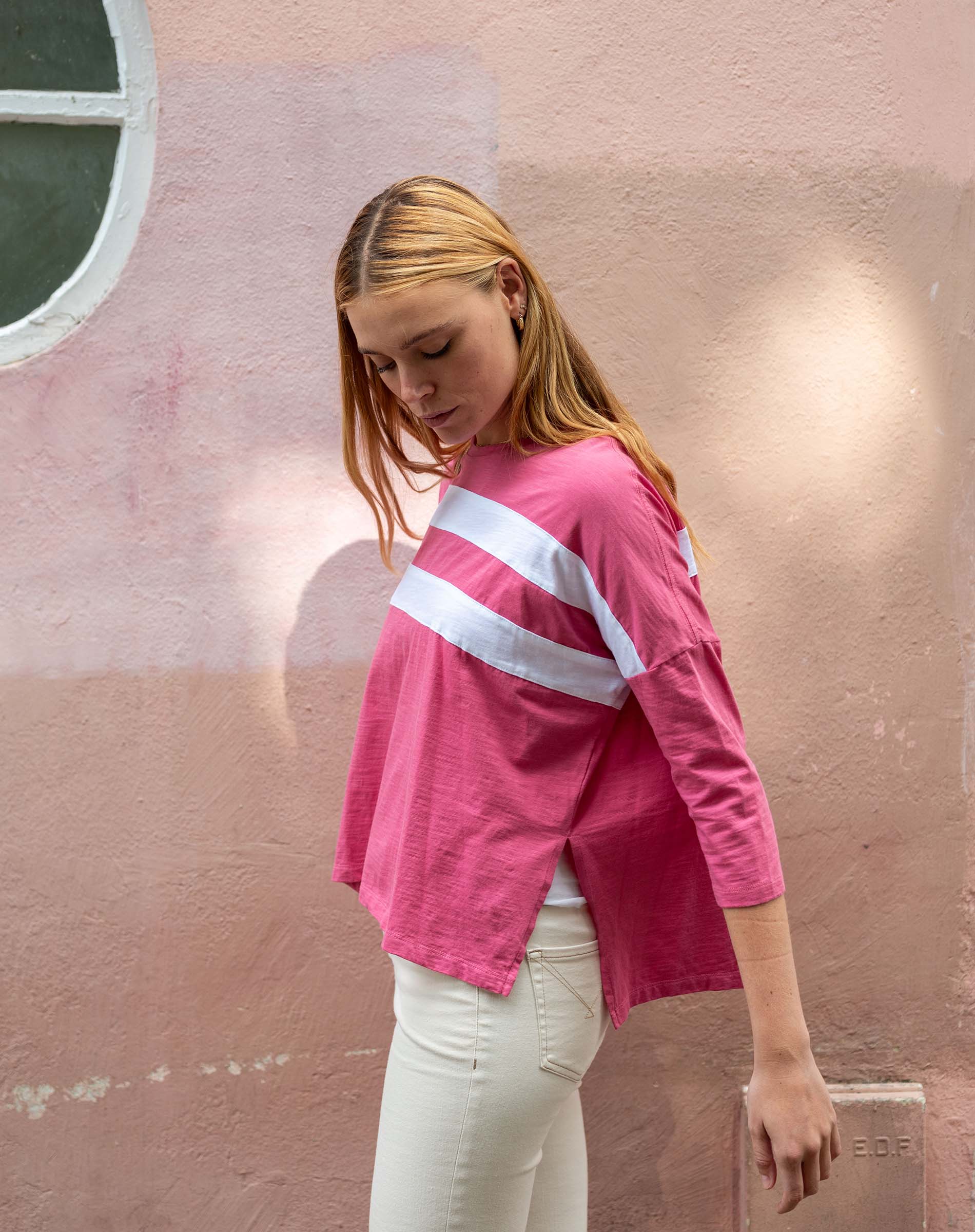 Woman wearing a pink long-sleeve shirt with a white stripe against a pink wall.