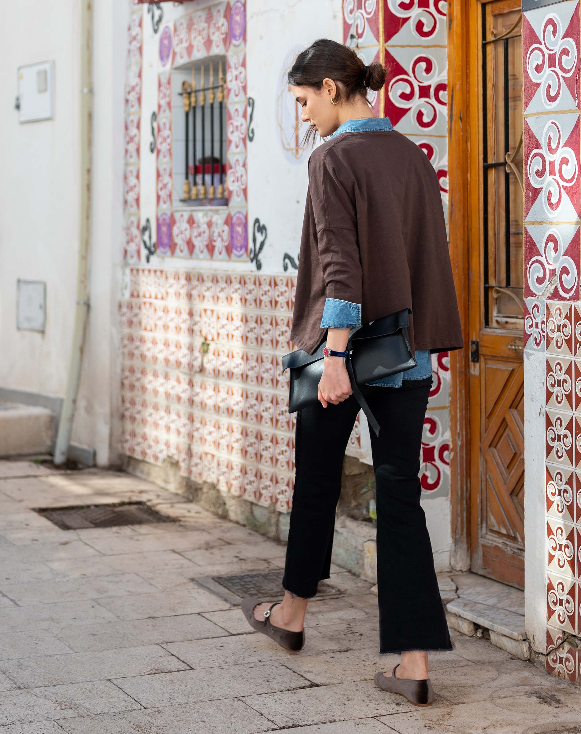 Model wearing an espresso brown slub knit top and black wide-leg trousers in a tiled courtyard.