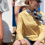 Woman in yellow and white striped shirt with colorful scarf sitting outdoors