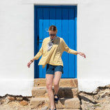 Woman in a yellow striped shirt and denim shorts standing in front of a blue door.