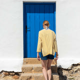 Woman in a yellow striped shirt walking up stone steps to a blue door.