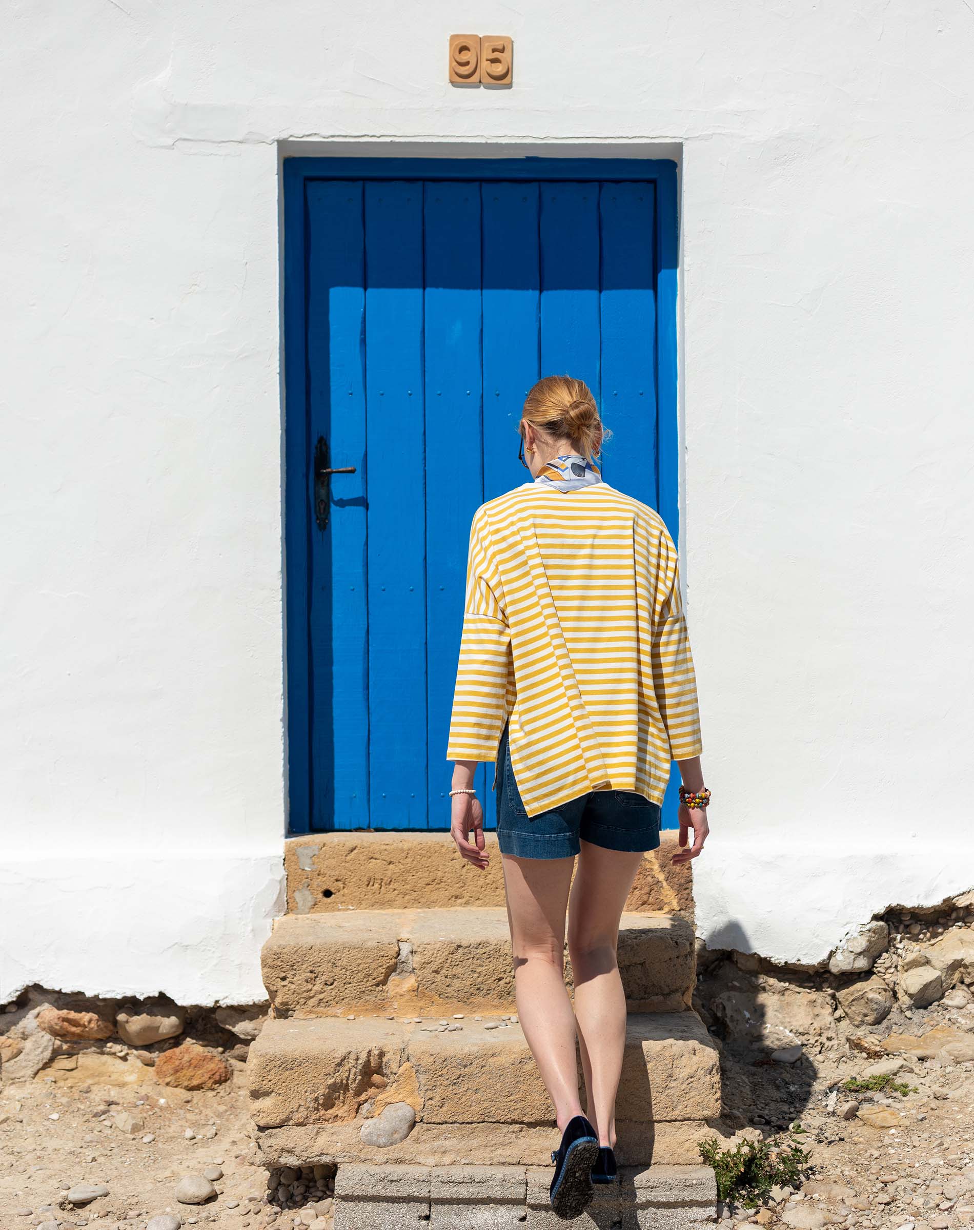 Woman in a yellow striped shirt walking up stone steps to a blue door.