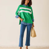 Woman wearing a green and white striped shirt with blue jeans, holding a beige bag.
