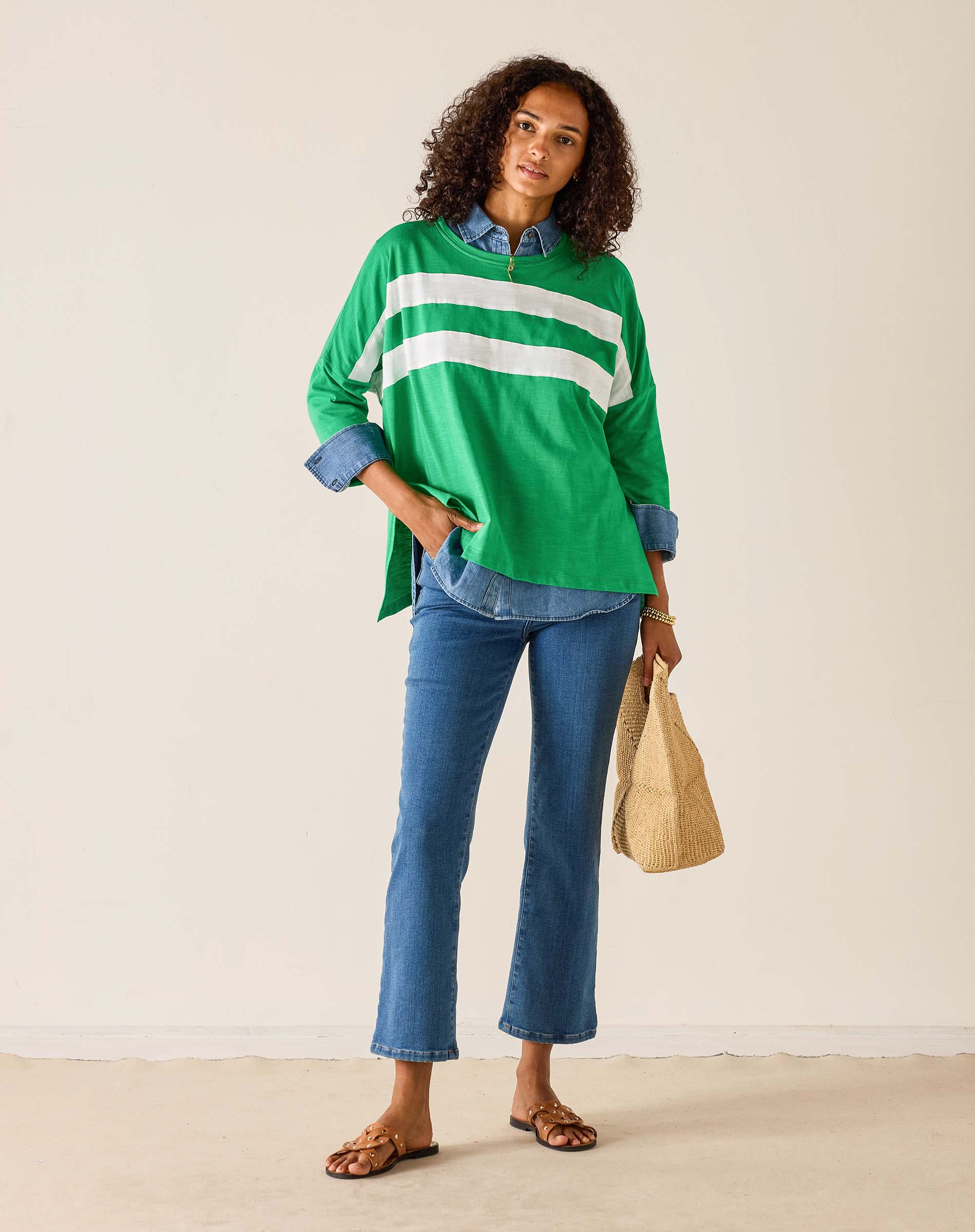 Woman wearing a green and white striped shirt with blue jeans, holding a beige bag.