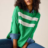 Woman wearing a green oversized shirt with white stripes and blue jeans, sitting on a beige background.
