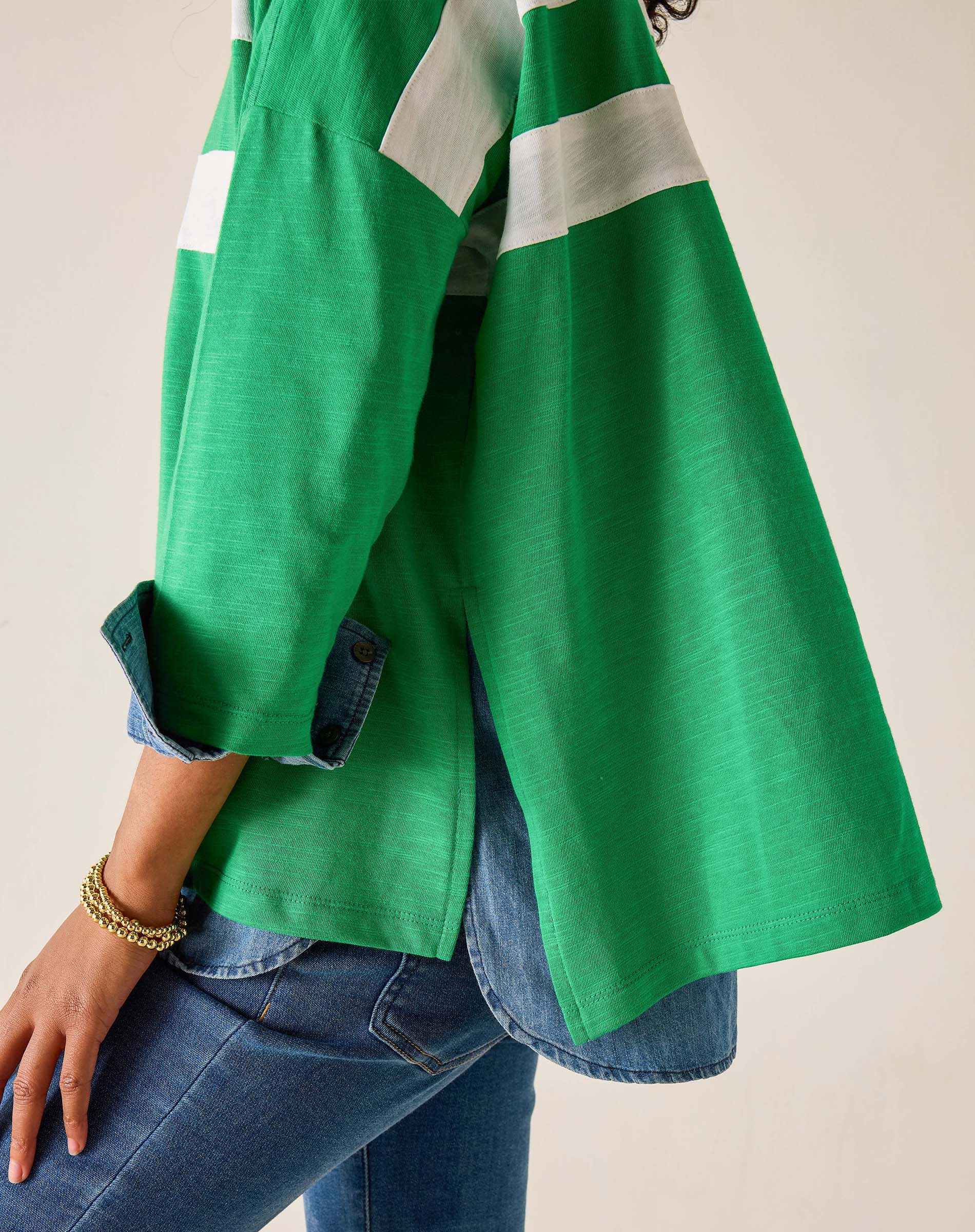 Green jacket with white stripes over a blue denim outfit on a neutral background