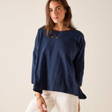 Woman wearing a navy blue top and white pants against a beige background