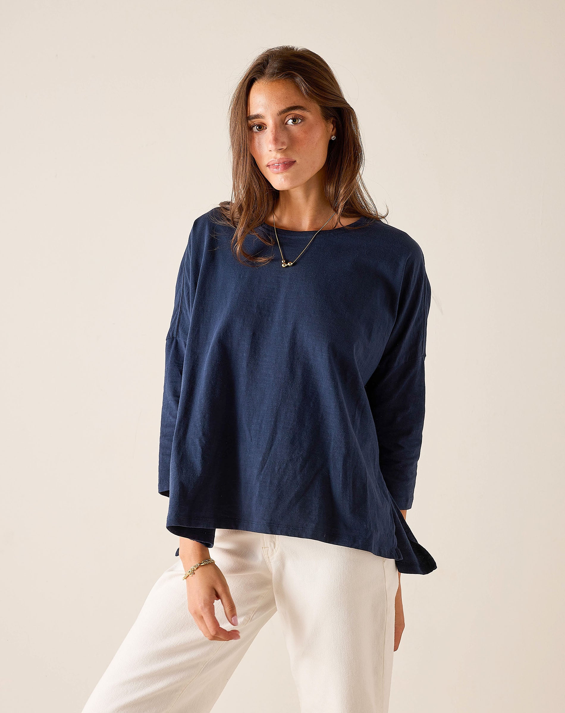 Woman wearing a navy blue top and white pants against a beige background