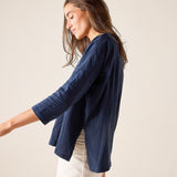 Woman wearing a navy blue top and white pants against a beige background