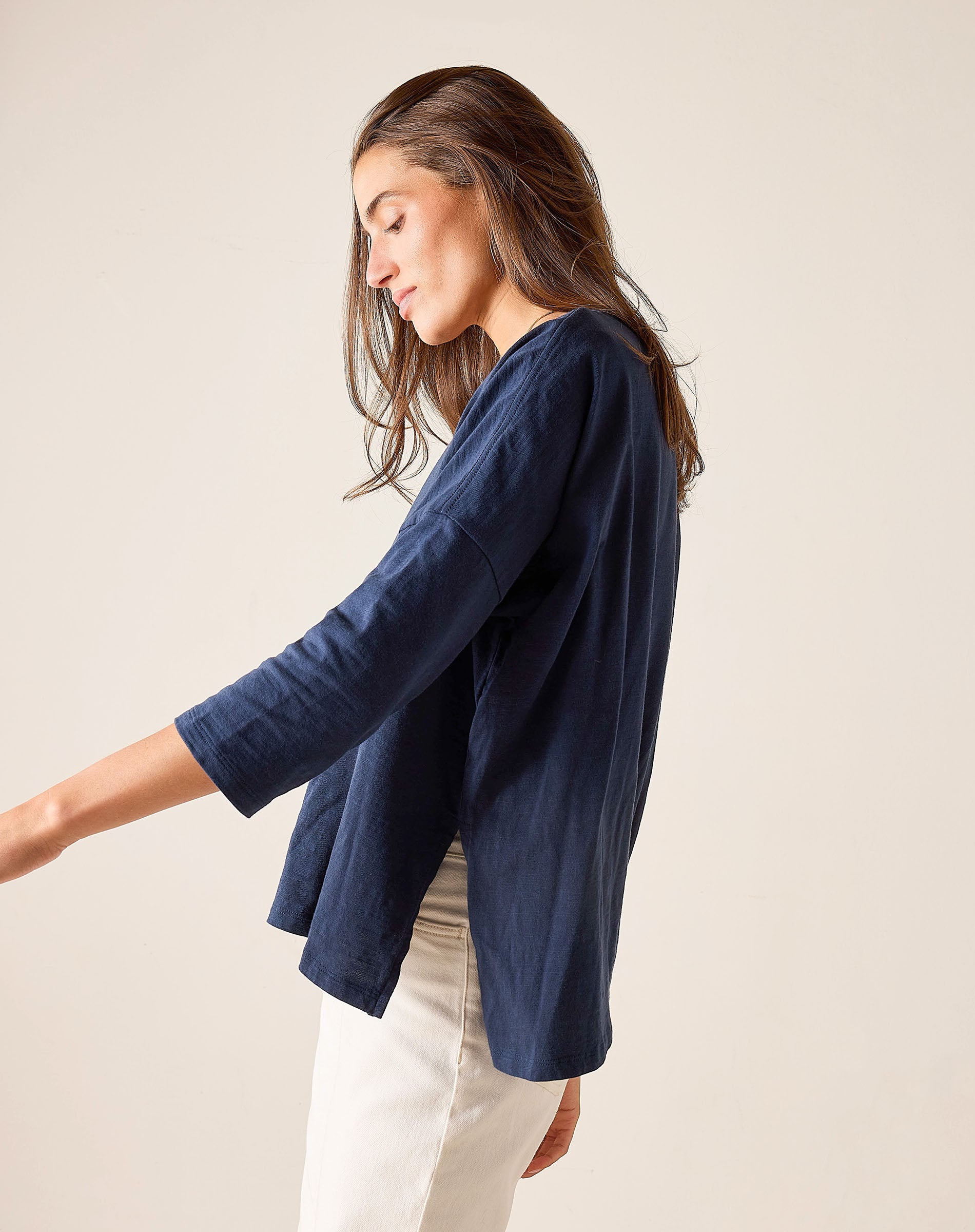 Woman wearing a navy blue top and white pants against a beige background
