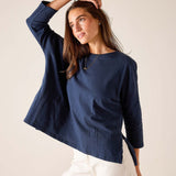 Woman wearing a navy blue top and white pants against a plain background