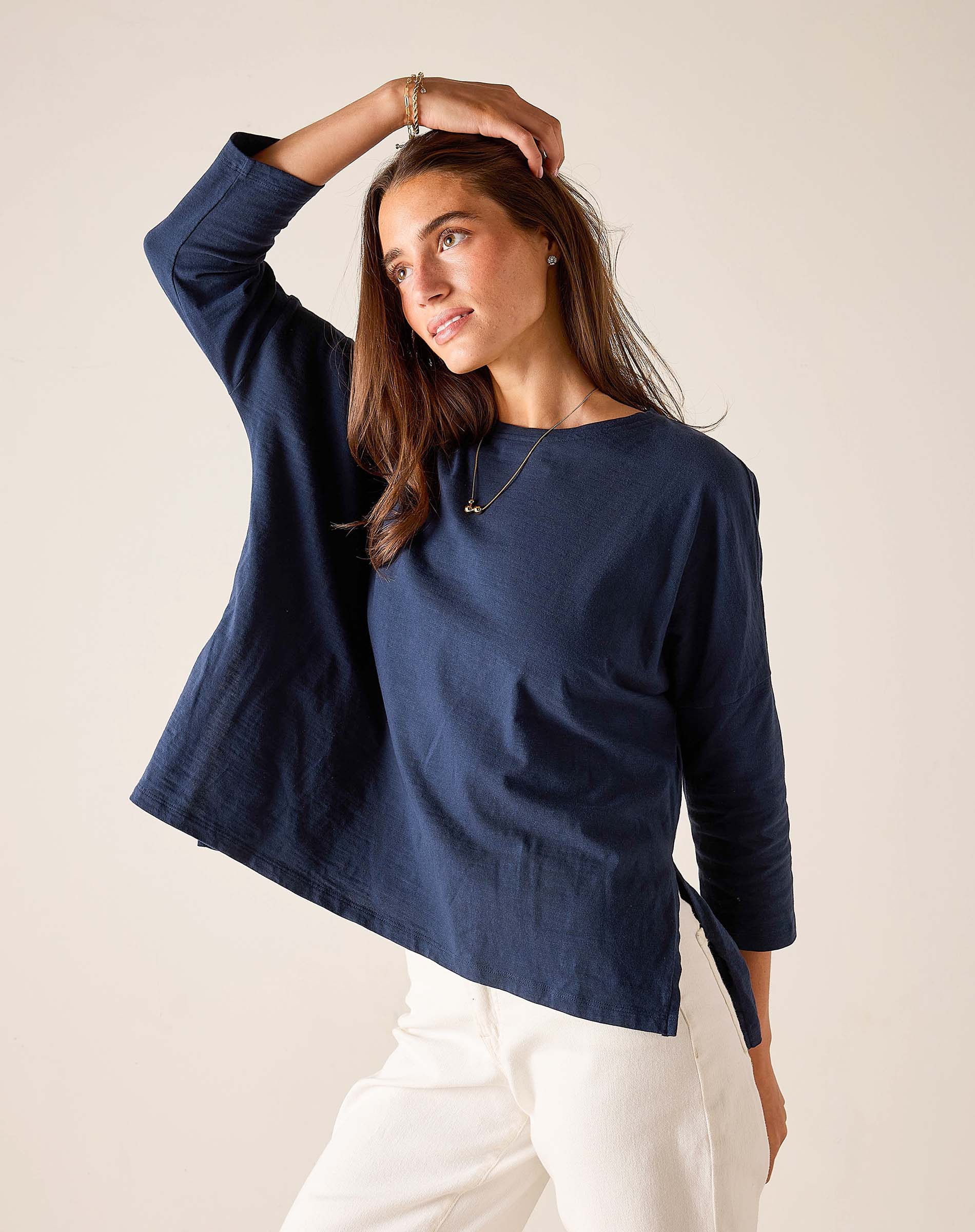Woman wearing a navy blue top and white pants against a plain background