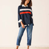 Woman wearing a navy sweater with red and white stripes and blue jeans on a plain background