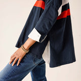 Person wearing a navy jacket with red and white stripes and blue jeans on a light background