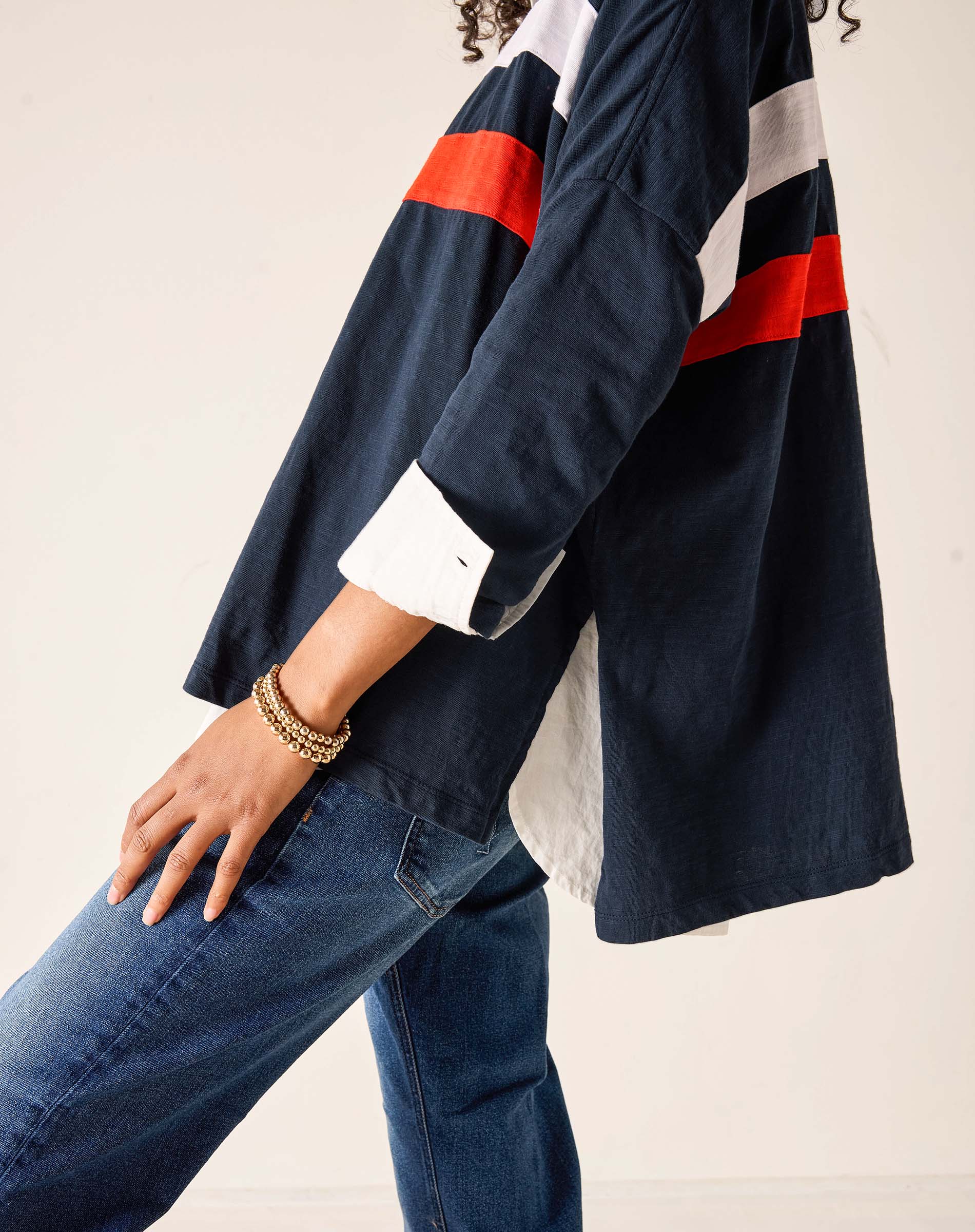 Person wearing a navy jacket with red and white stripes and blue jeans on a light background