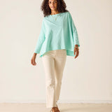 Woman wearing a light green top and beige pants against a white background
