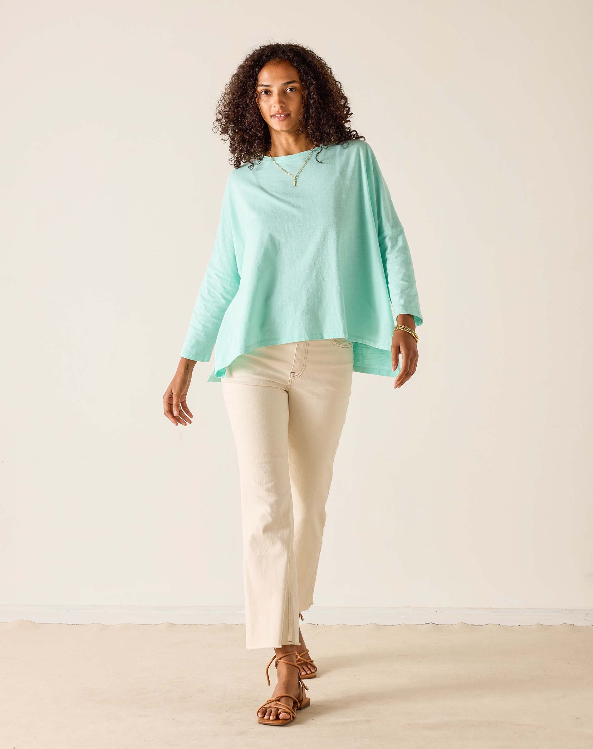 Woman wearing a light green top and beige pants against a white background